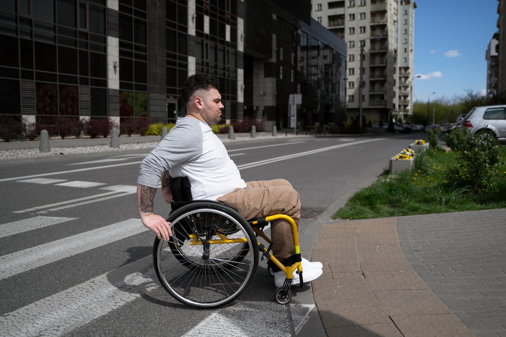Homem cadeirante subindo em uma calçada com rampa, representando as cidades acessíveis.