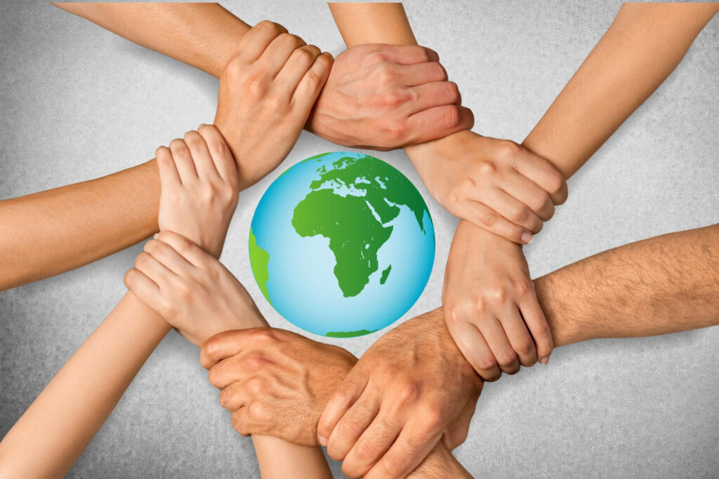 Pessoas em volta da miniatura do globo terrestre com os braços entrelaçados uns nos outros para cumprir os objetivos de desenvolvimento sustentável.